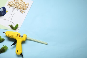 Hot glue gun and handicraft materials on light blue background, flat lay. Space for text