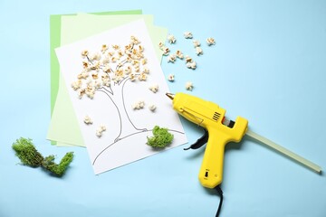 Hot glue gun and handicraft materials on light blue background, flat lay