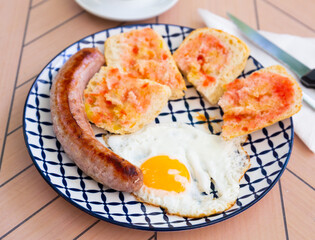 Delicious and hearty breakfast of fried eggs with sausage and fresh baguette slices dressed with vegetable sauce