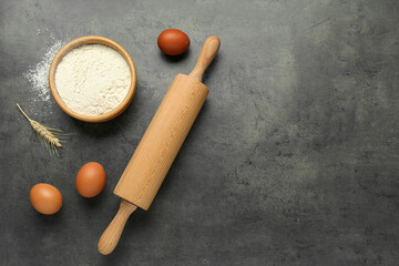 Rolling pin, bowl of flour, eggs and spike on grey table, flat lay. Space for text