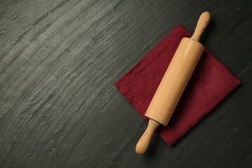 Wooden rolling pin and napkin on dark gray textured table, top view. Space for text