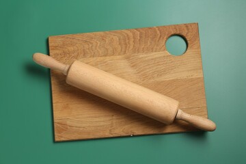Rolling pin and wooden board on green background, top view