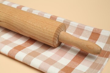 Wooden rolling pin and checkered napkin on beige background, closeup