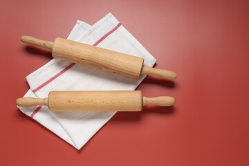 Wooden rolling pins and napkin on red background, flat lay