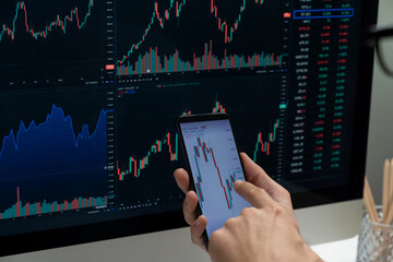 Smart stock investors pointing on screen with smartphone for market stock exchange along with laptop screen in highest dynamic investment rate, focusing data planning at modern workplace. Pecuniary.