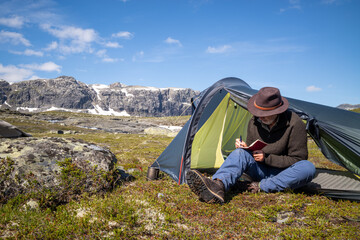 Hiking maie sitting in his tent opening writing in a notebook