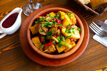 Appetizing spicy Ojakhuri from roasted pork with potatoes and onions garnished with fresh greens served with pomegranate sauce in traditional clay ketsi pan. Authentic Georgian cuisine