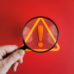 Cybersecurity Alert: Magnifying Glass Reveals Glowing Exclamation Mark Warning Sign on Red...