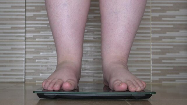 Fat legs end up on the scales. A man stands on a scale and tries to cheat the scale by lifting his foot. Disappointment from the result on the scales. Anger at his own weight. Video in the bathroom.