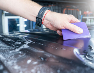 A car wrapping specialist applies a polyurethane film to the car. Selective focus. PPF protective film against chips and scratches. Car wrapping, tuning, styling. 