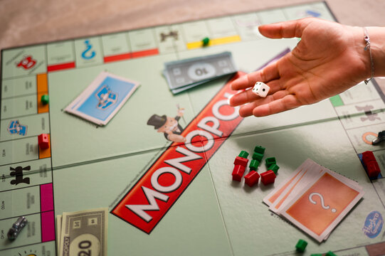 Monopoly Board Game in Progress: Close-up Shot of Player Rolling Dice onto the Board with Chance Cards, Currency, and Game Pieces Visible
