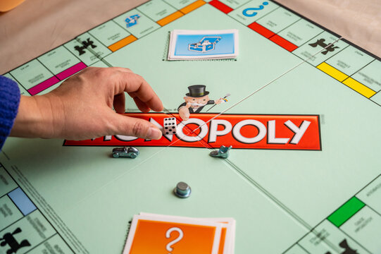 Monopoly Game in Progress: Close-up of Player's Hand on the Board with Mr. Monopoly Logo, Chance Card, and Game Pieces Visible, Emphasizing the Interaction and Movement Around the Board.