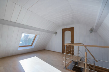 Fototapeta premium Attic decorated with wood and painted white. Stairs with wooden railings, a door with glass windows. Unfurnished.