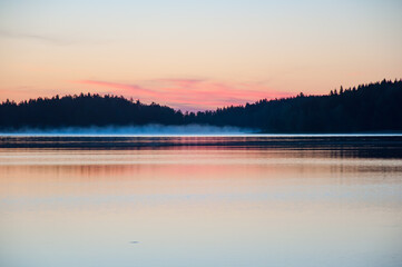 Early summer night by a calm lake in Finland with fog rising from the water