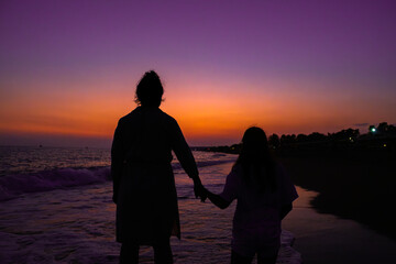 Fototapeta premium Picture of daughter with mother in the waves of the Turkish Sea at an orange sunset.