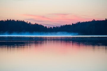 Early summer night by a calm lake in Finland with fog rising from the water