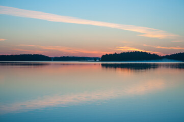 Early summer night by a calm lake in Finland with fog rising from the water
