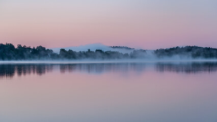 Fototapeta premium Early summer night by a calm lake in Finland with fog rising from the water