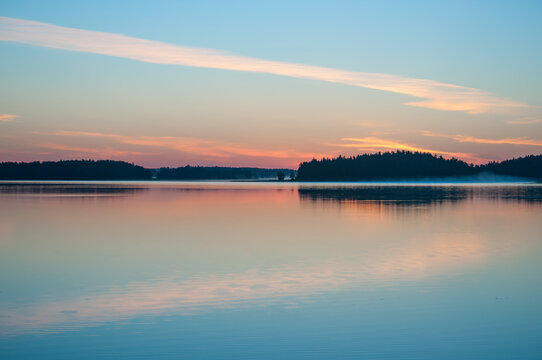 Early summer night by a calm lake in Finland with fog rising from the water