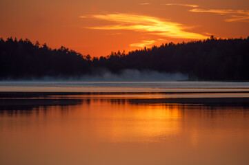 Early summer night by a calm lake in Finland with fog rising from the water