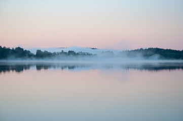 Early summer night by a calm lake in Finland with fog rising from the water