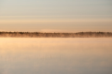 Early summer night by a calm lake in Finland with fog rising from the water