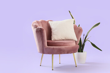 Beautiful pink armchair with houseplant and pillows on lilac background