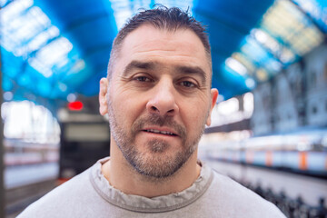  Close-up of a middle-aged man in a gray sweatshirt gazing upward at a train station. His...