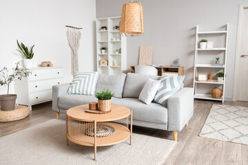 Interior of light living room with grey sofa, coffee table and shelf units