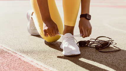 Training, Healthy Lifestyle Concept. Closeup cropped view of unrecognizable African American woman in yellow leggings tying her shoelaces before jogging outdoors in the morning, wearing white sneakers