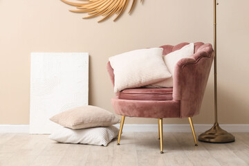 Stylish pink armchair with soft cushions, standard lamp and mirror near beige wall
