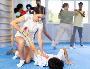 Focused teenage girl learning effective self defence techniques in sparring with boy, practicing...