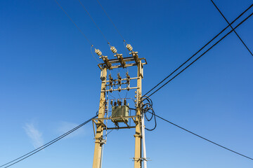 Electrical power transformer mounted on a utility pole with wires against a clear blue sky.