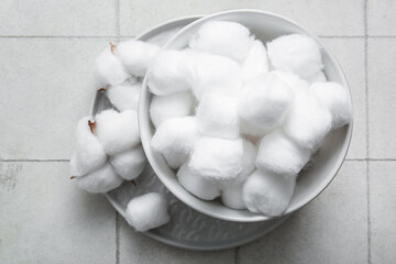 Bowl and plate with cotton balls and flowers on white tile background