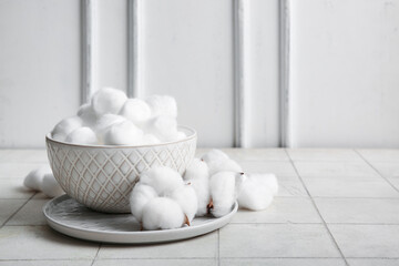 Bowl and plate with cotton balls and flowers on white tile table