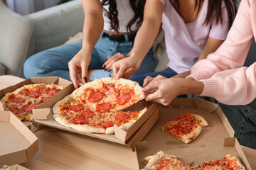 Female friends taking slices of pepperoni pizza at home, closeup