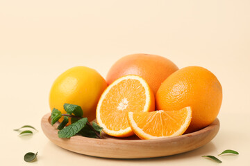 Wooden plate with cut citrus fruits and mint leaves on beige background