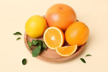 Wooden plate with cut citrus fruits and mint leaves on beige background