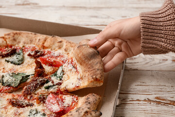 Female hand taking slice of delicious pizza Margarita on white wooden background. Closeup