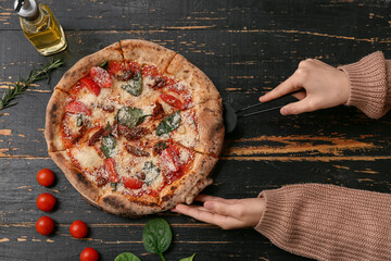 Female hands taking slice of tasty pizza Margarita on black wooden background. Top view