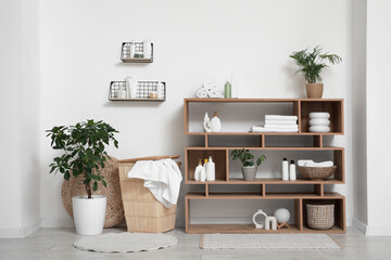 Fototapeta premium Basket with towels and cosmetic products on shelving unit near white wall in bathroom