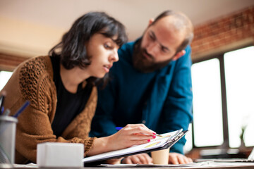 Caucasian female analyst holding clipboard and explaining market analysis result to male coworker with beard. Closeup on businesswoman and man researching startup company financial documents at desk.