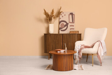 Interior of living room with armchair, coffee table and home decor on commode near brown wall