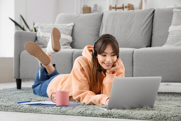 Teenage girl in headset with laptop working online on carpet at home