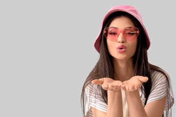 Young woman blowing kiss on grey background, closeup