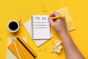 Male hand with to-do list, notebooks, cup of coffee and stationery on yellow background