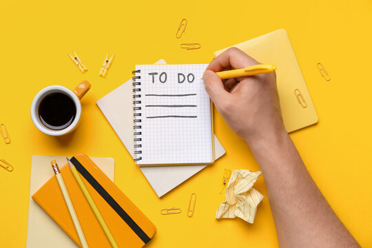 Male hand with to-do list, notebooks, cup of coffee and stationery on yellow background