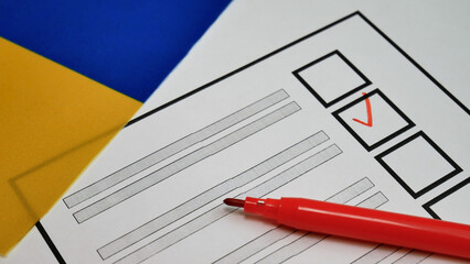 Democracy in action during Ukraine elections. Voters hand holds red marker, placing checkmark next to candidate. Ukrainian flag in background. Election integrity, political freedom, voting rights