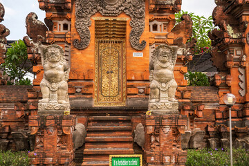 Detailed guardian figures stand watch at a Balinese temple gate, featuring a dazzling gold door. The intricate carvings and vibrant colors of the brickwork highlight Balinese artistry and tradition.