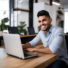 Un joven hispano sonríe ante la cámara con cara de feliz en su despacho con un laptop